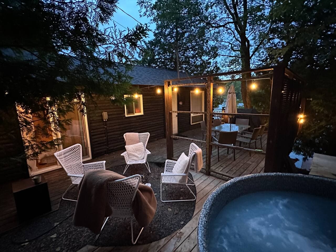 Twilight deck patio with hot tub, lounge chairs and string lights by the cottage.